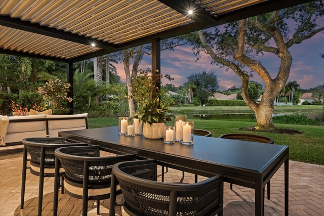 patio terrace at dusk featuring outdoor dining area and a lawn
