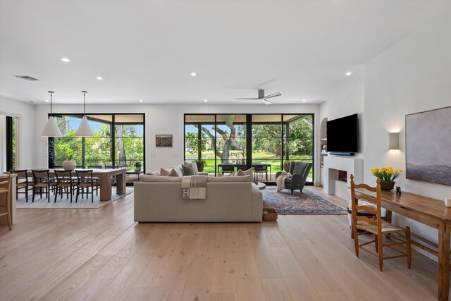 living area featuring light wood-style flooring, recessed lighting, a warm lit fireplace, and ceiling fan