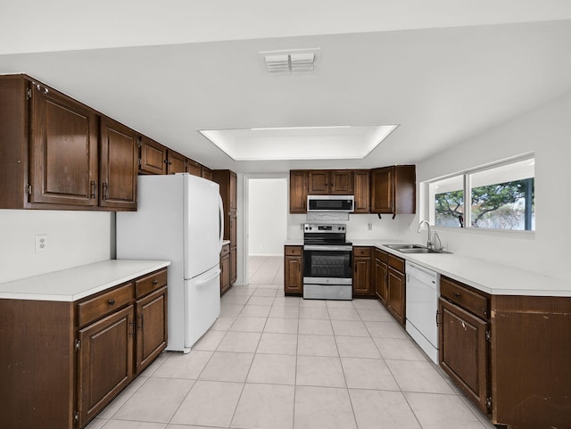 kitchen with appliances with stainless steel finishes, a sink, dark brown cabinets, light countertops, and light tile patterned floors