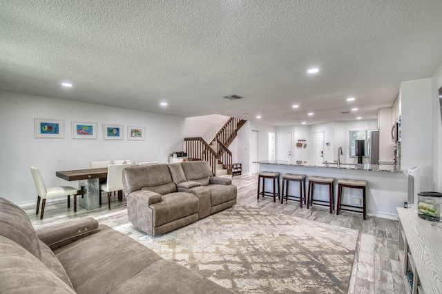 living room with stairs, a textured ceiling, light wood-type flooring, and recessed lighting