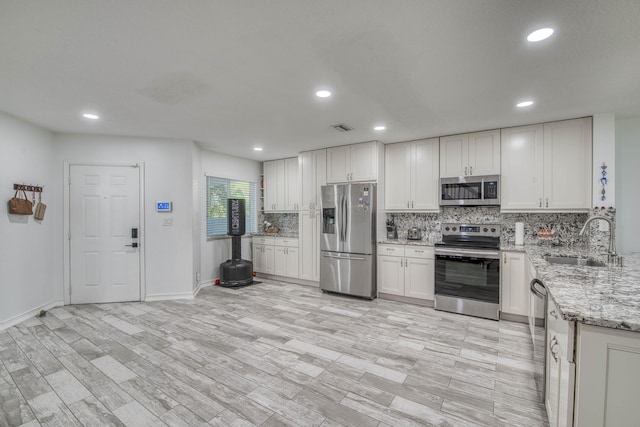 kitchen with a sink, visible vents, backsplash, appliances with stainless steel finishes, and light stone counters