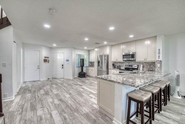 kitchen featuring a peninsula, light wood-style flooring, a sink, appliances with stainless steel finishes, and light stone counters