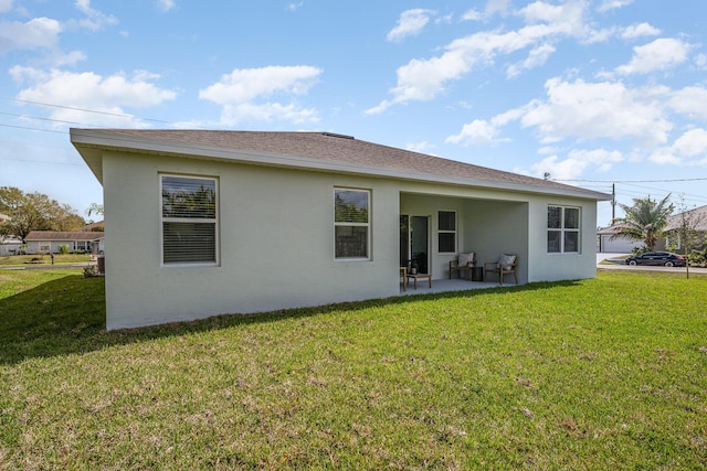 rear view of property featuring a lawn, a patio area, stucco siding, and a shingled roof
