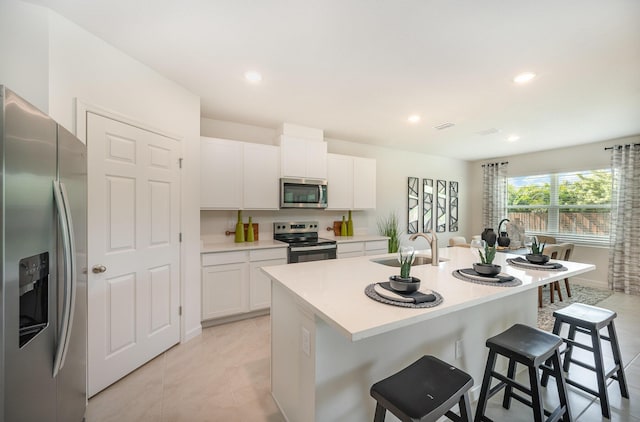 kitchen with a sink, a kitchen breakfast bar, a center island with sink, stainless steel appliances, and white cabinets