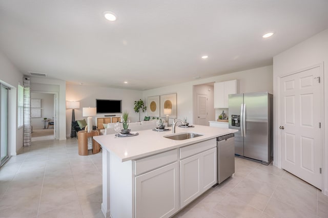 kitchen featuring an island with sink, a sink, stainless steel appliances, white cabinetry, and light countertops