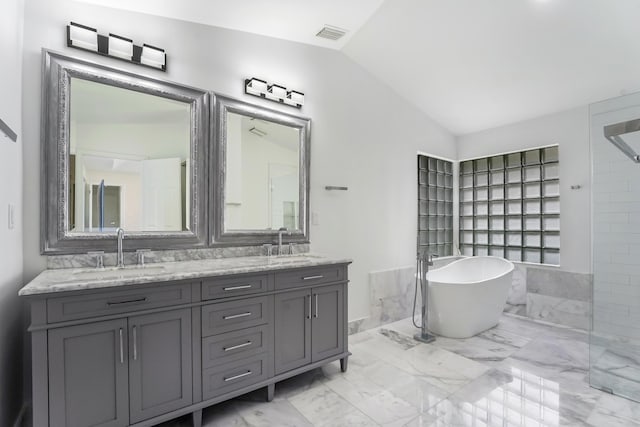 full bathroom featuring marble finish floor, a freestanding bath, a sink, and vaulted ceiling