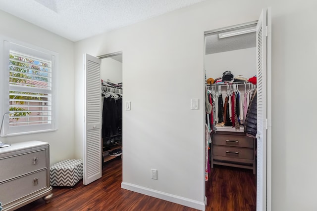 bedroom with a textured ceiling, dark wood-type flooring, baseboards, and a walk in closet
