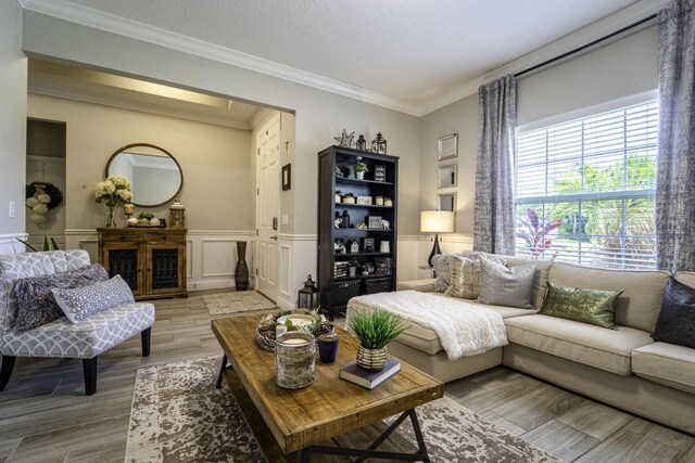 living room with light wood-style floors, crown molding, a wainscoted wall, and a decorative wall