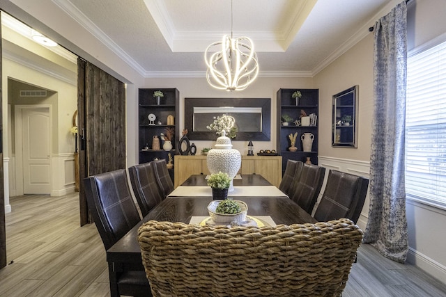 dining area with crown molding, wainscoting, a raised ceiling, a notable chandelier, and light wood-style floors