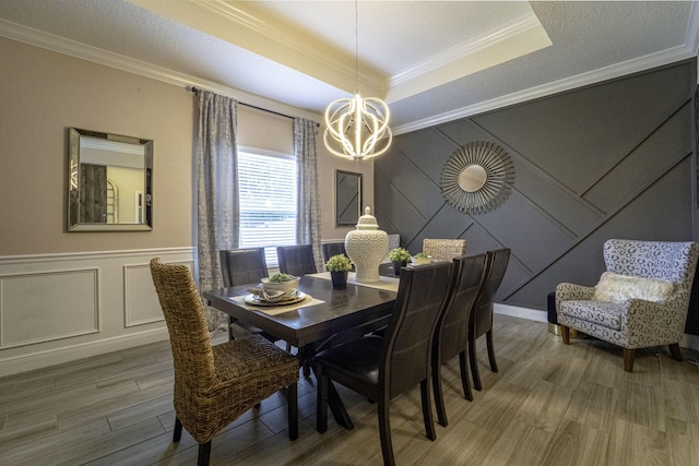 dining area featuring a decorative wall, crown molding, a tray ceiling, a notable chandelier, and light wood-style floors