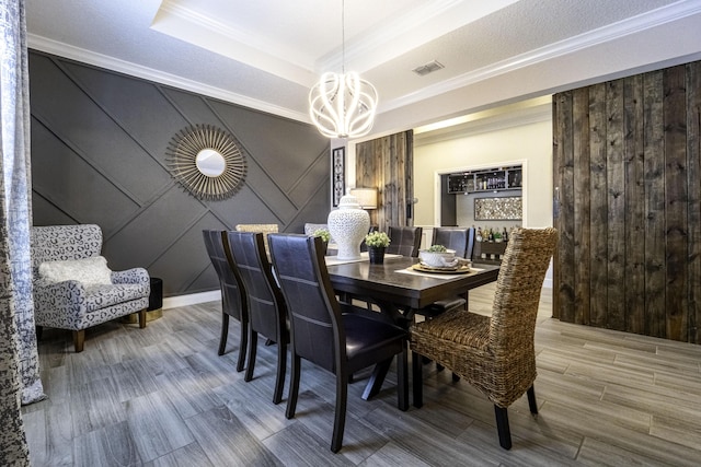 dining area with a chandelier, a tray ceiling, wood finished floors, crown molding, and a decorative wall