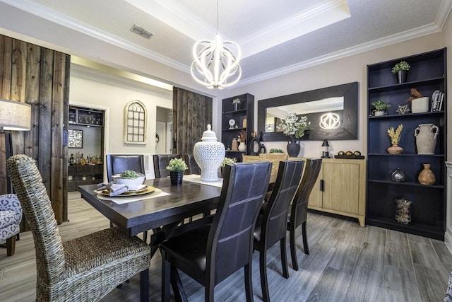 dining room featuring a tray ceiling, light wood finished floors, an inviting chandelier, built in features, and crown molding
