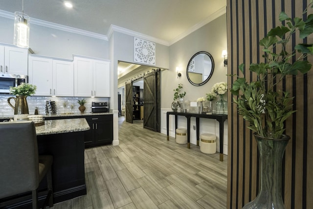 kitchen featuring light stone countertops, light wood-style flooring, stainless steel microwave, white cabinets, and tasteful backsplash