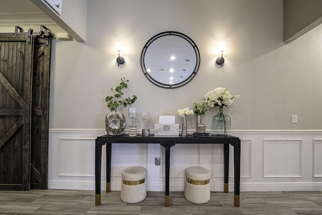 interior space with a decorative wall, wood finished floors, a barn door, and wainscoting