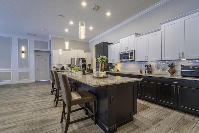 kitchen with a sink, crown molding, visible vents, appliances with stainless steel finishes, and decorative backsplash