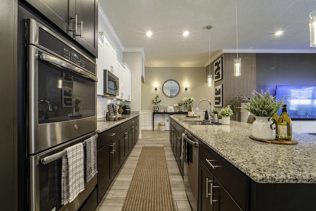 kitchen featuring ornamental molding, light stone counters, a sink, stainless steel appliances, and a large island with sink