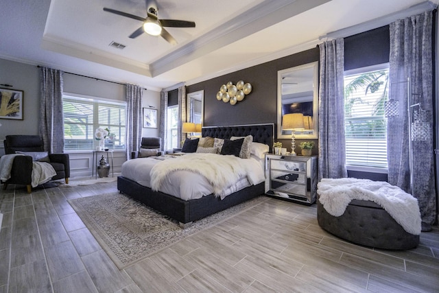 bedroom with ceiling fan, visible vents, crown molding, wood finish floors, and a raised ceiling