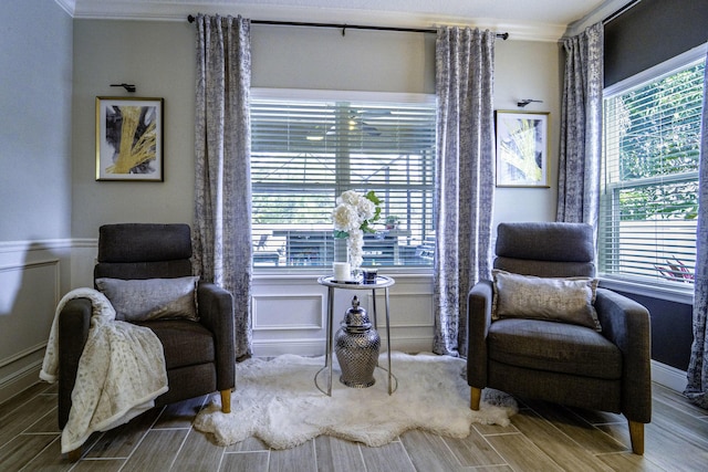 living area featuring ornamental molding, wood tiled floor, a decorative wall, and a wainscoted wall