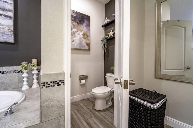 bathroom with toilet, baseboards, and wood finished floors