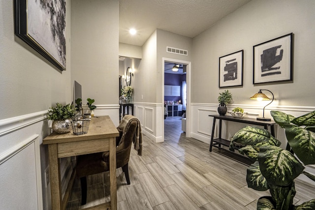 dining area featuring a textured ceiling, visible vents, light wood-style flooring, and wainscoting