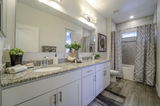 bathroom with double vanity, shower / bath combination with curtain, toilet, and a sink
