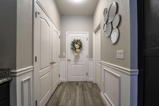 doorway to outside with a wainscoted wall, a textured ceiling, and wood tiled floor