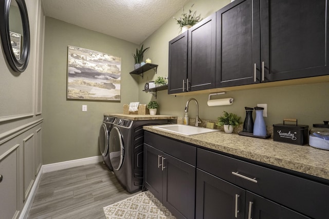 washroom featuring a textured ceiling, a sink, washer and clothes dryer, light wood-type flooring, and cabinet space