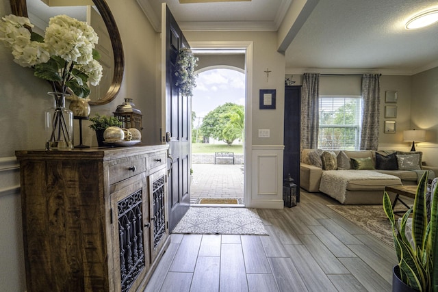 foyer entrance with crown molding, a wainscoted wall, light wood-style flooring, and a decorative wall