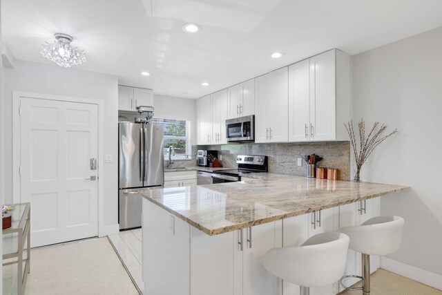 701 NE Harbour Ter Unit 103, Boca Raton, FL 33431 - kitchen featuring appliances with stainless steel finishes, a peninsula, light stone countertops, backsplash, and baseboards