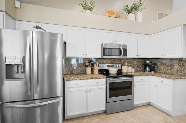 kitchen with stainless steel appliances, decorative backsplash, dark stone counters, and white cabinets