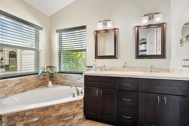 bathroom featuring double vanity, a bath, vaulted ceiling, and a sink