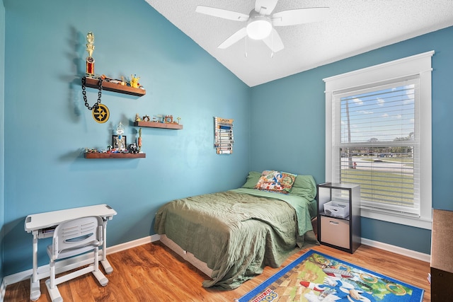 bedroom featuring wood finished floors, a ceiling fan, a textured ceiling, baseboards, and lofted ceiling