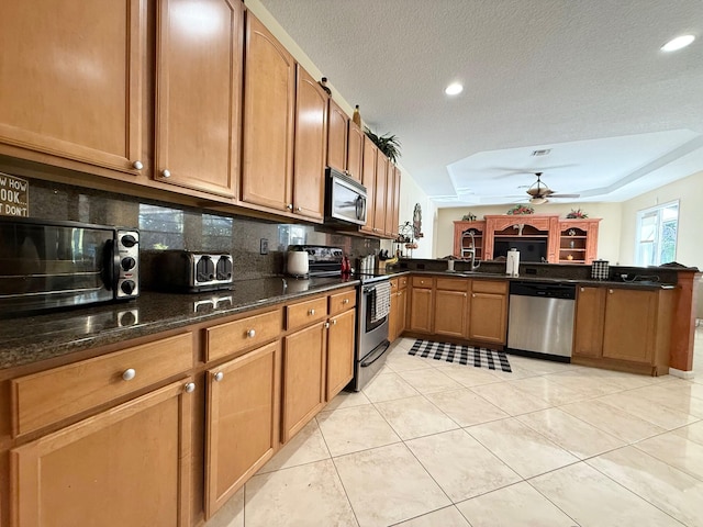 kitchen with a peninsula, a ceiling fan, a sink, backsplash, and appliances with stainless steel finishes
