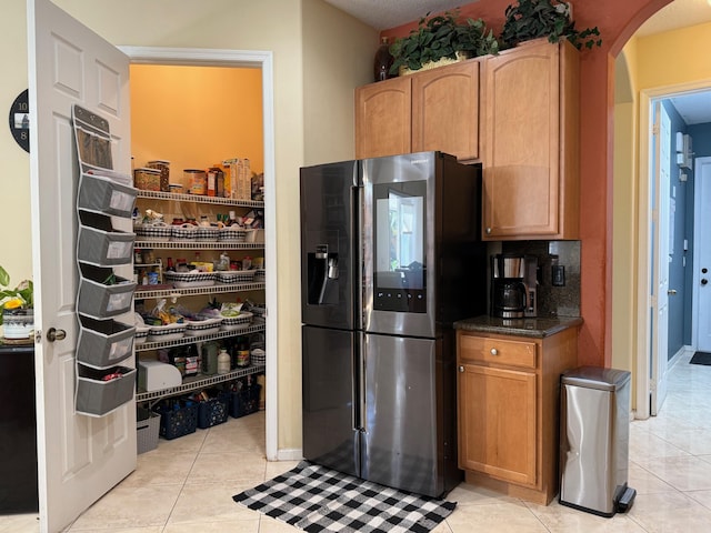 kitchen with stainless steel fridge with ice dispenser, arched walkways, light tile patterned floors, and dark stone counters