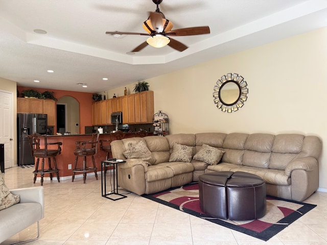 living area with a ceiling fan, a raised ceiling, arched walkways, light tile patterned flooring, and recessed lighting
