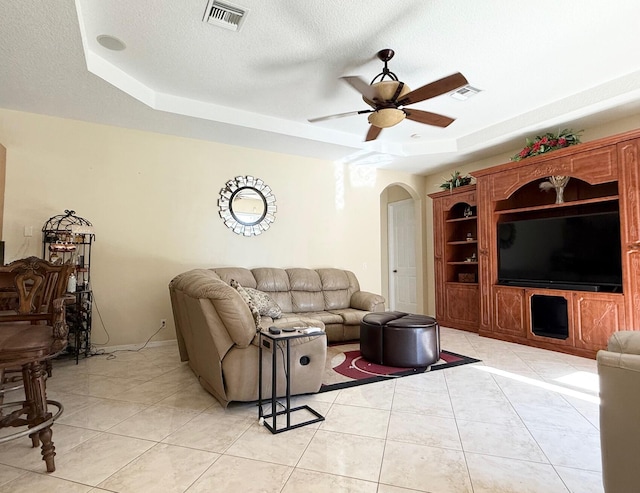 living area with visible vents, arched walkways, a ceiling fan, light tile patterned floors, and a raised ceiling