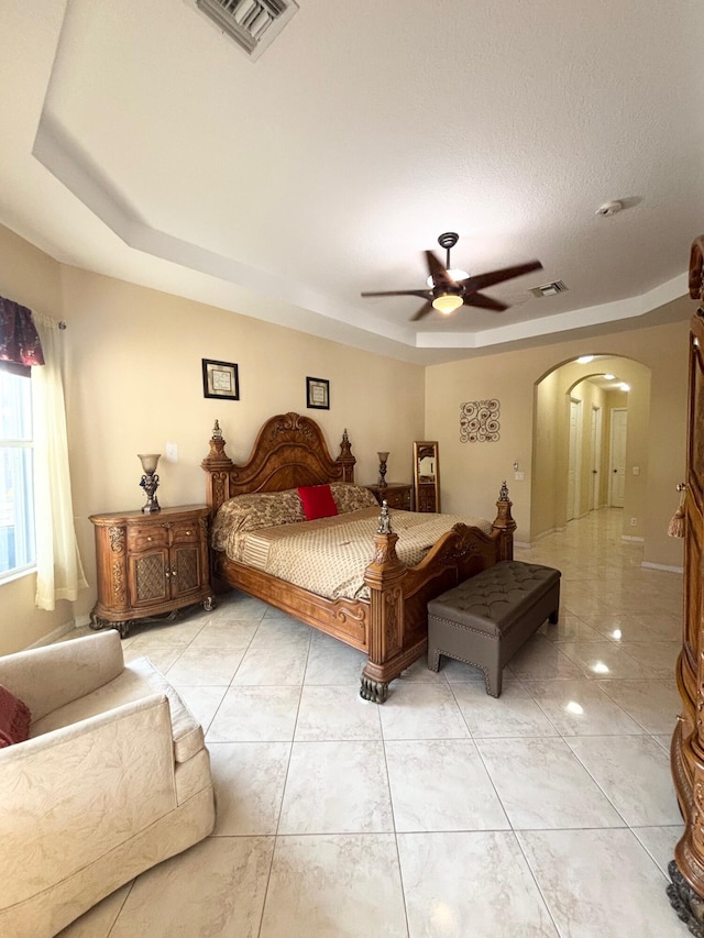 bedroom featuring arched walkways, a raised ceiling, visible vents, and a ceiling fan