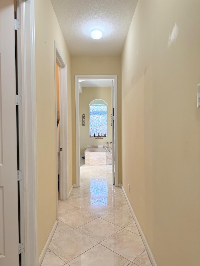 hall featuring a textured ceiling and baseboards