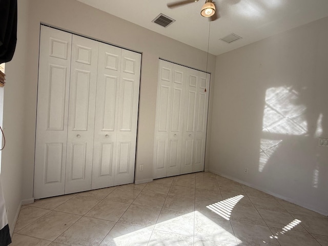 unfurnished bedroom with light tile patterned floors, ceiling fan, visible vents, and two closets