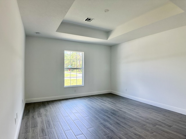 empty room featuring a raised ceiling, baseboards, visible vents, and dark wood finished floors