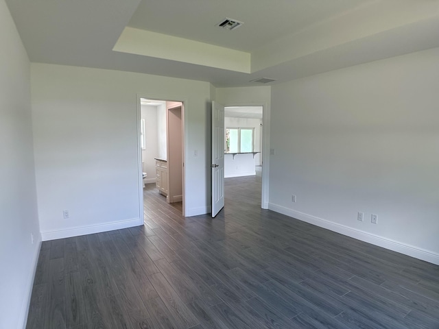 unfurnished room featuring baseboards, dark wood finished floors, a tray ceiling, and visible vents