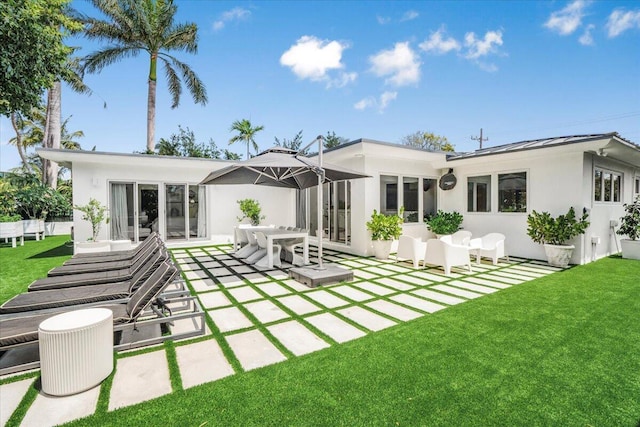 back of property with a patio, stucco siding, a standing seam roof, and a lawn