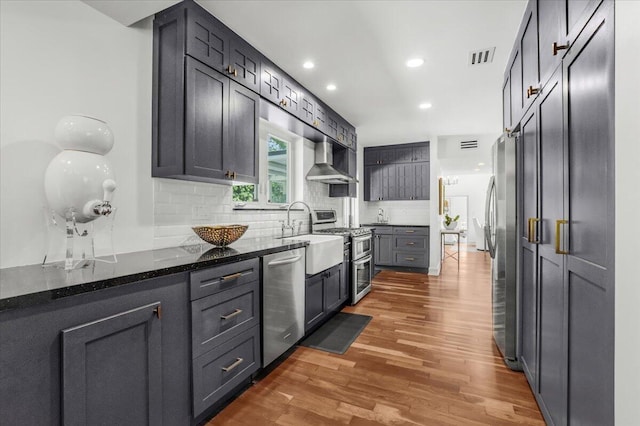 6100 La Gorce Dr, Miami Beach, FL 33140 - kitchen with appliances with stainless steel finishes, wall chimney range hood, light wood finished floors, decorative backsplash, and recessed lighting