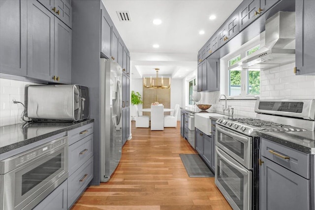 6100 La Gorce Dr, Miami Beach, FL 33140 - kitchen with stainless steel appliances, wall chimney exhaust hood, light wood-type flooring, backsplash, and recessed lighting
