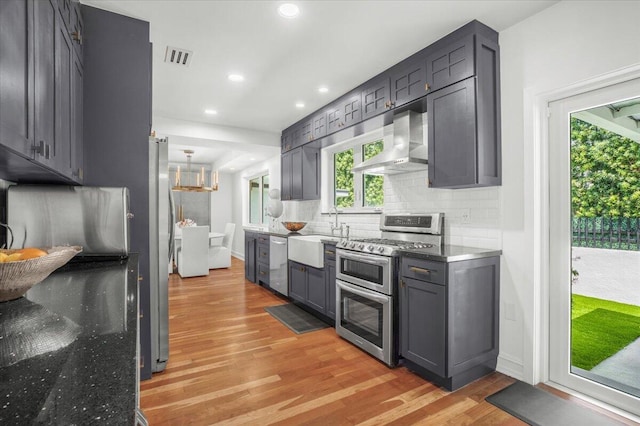 6100 La Gorce Dr, Miami Beach, FL 33140 - kitchen with appliances with stainless steel finishes, wall chimney exhaust hood, a sink, light wood-type flooring, and decorative backsplash