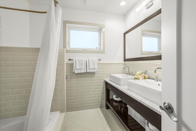 full bath featuring tile walls, tile patterned floors, a sink, and a wealth of natural light