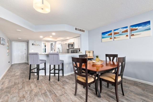 dining area with baseboards, visible vents, a textured ceiling, and wood finished floors