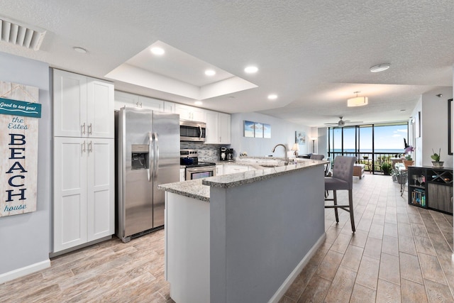 kitchen featuring a peninsula, light wood-style flooring, stainless steel appliances, white cabinets, and baseboards