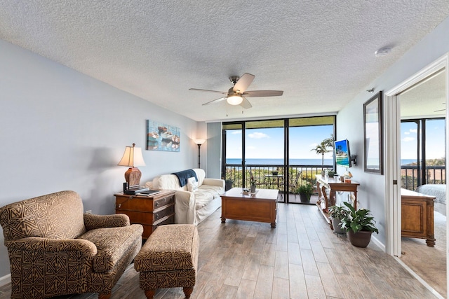 living area featuring light wood finished floors, a textured ceiling, expansive windows, baseboards, and ceiling fan