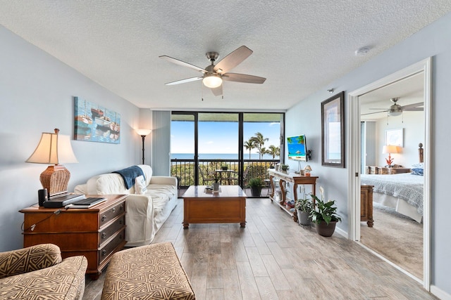living room with a textured ceiling, ceiling fan, floor to ceiling windows, and wood finished floors